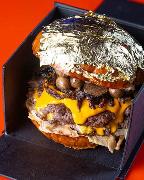 Stacked double cheeseburger crowned with gold leaf, in a black box on a red background