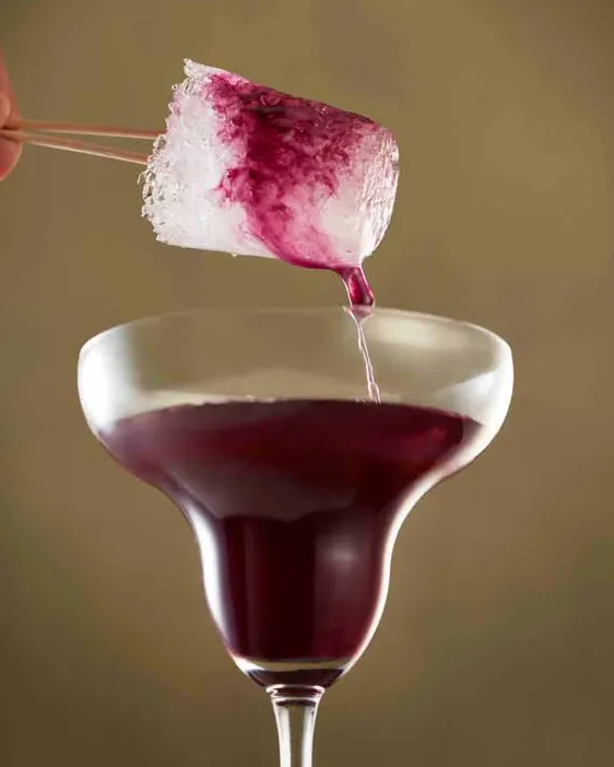 Ice-lolly chuski dripping purple syrup into a margarita glass of deep red cocktail