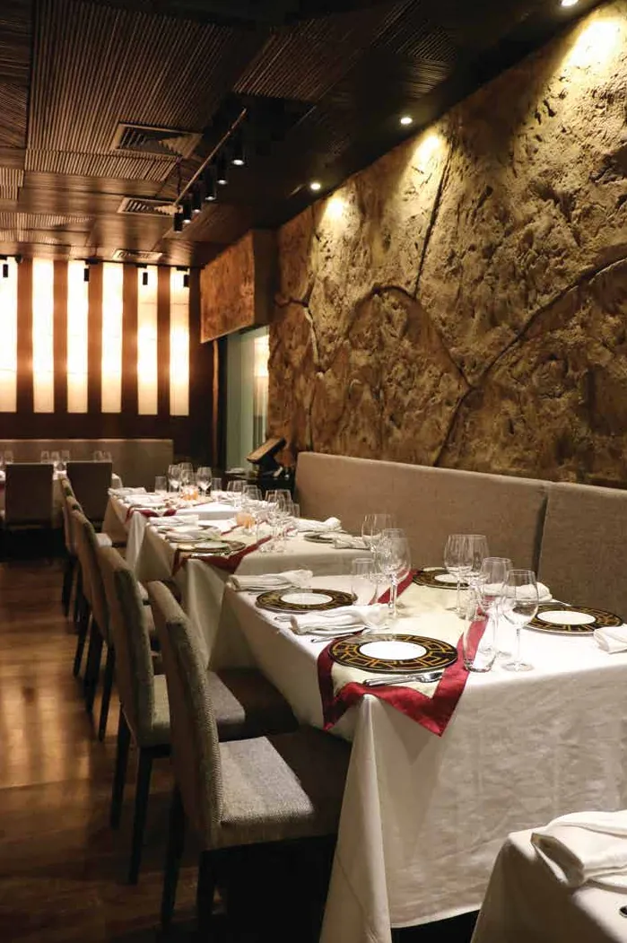 Long banquette dining row set with white linen beside a textured stone wall