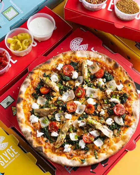 Round pizza with spinach, cherry tomatoes and feta on a red Slyce box
