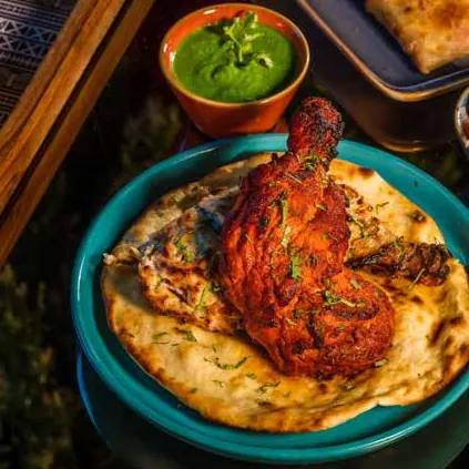 Tandoori chicken leg on naan in a teal bowl with green chutney